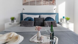 Une chambre à coucher bien rangée, avec un lit, des tables de chevet, un plateau avec une bouteille et des verres, et une décoration murale sur le thème de la plage.