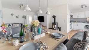 Une cuisine moderne avec des armoires blanches, une cuisinière encastrée et un coin repas doté d’une table en bois, mise pour quatre personnes.
