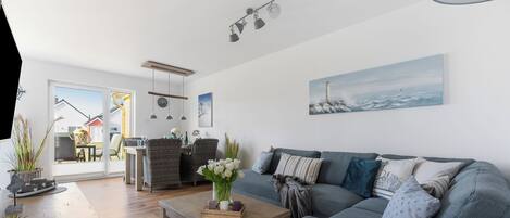 Una sala de estar moderna con un sofá gris, una mesa de centro de madera y vistas al exterior a través de un ventanal.
