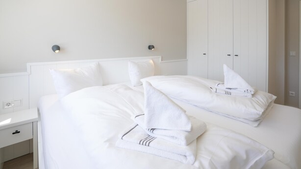 A hotel room with a neatly made bed, white walls, and a large wardrobe.