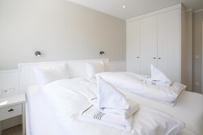 A hotel room with a neatly made bed, white walls, and a large wardrobe. - Ankerkoje, Haus Ankerlicht, App. 57 (Sylt)