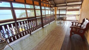 Un balcone coperto con pavimento in legno, ringhiere in metallo e vista sul mare.