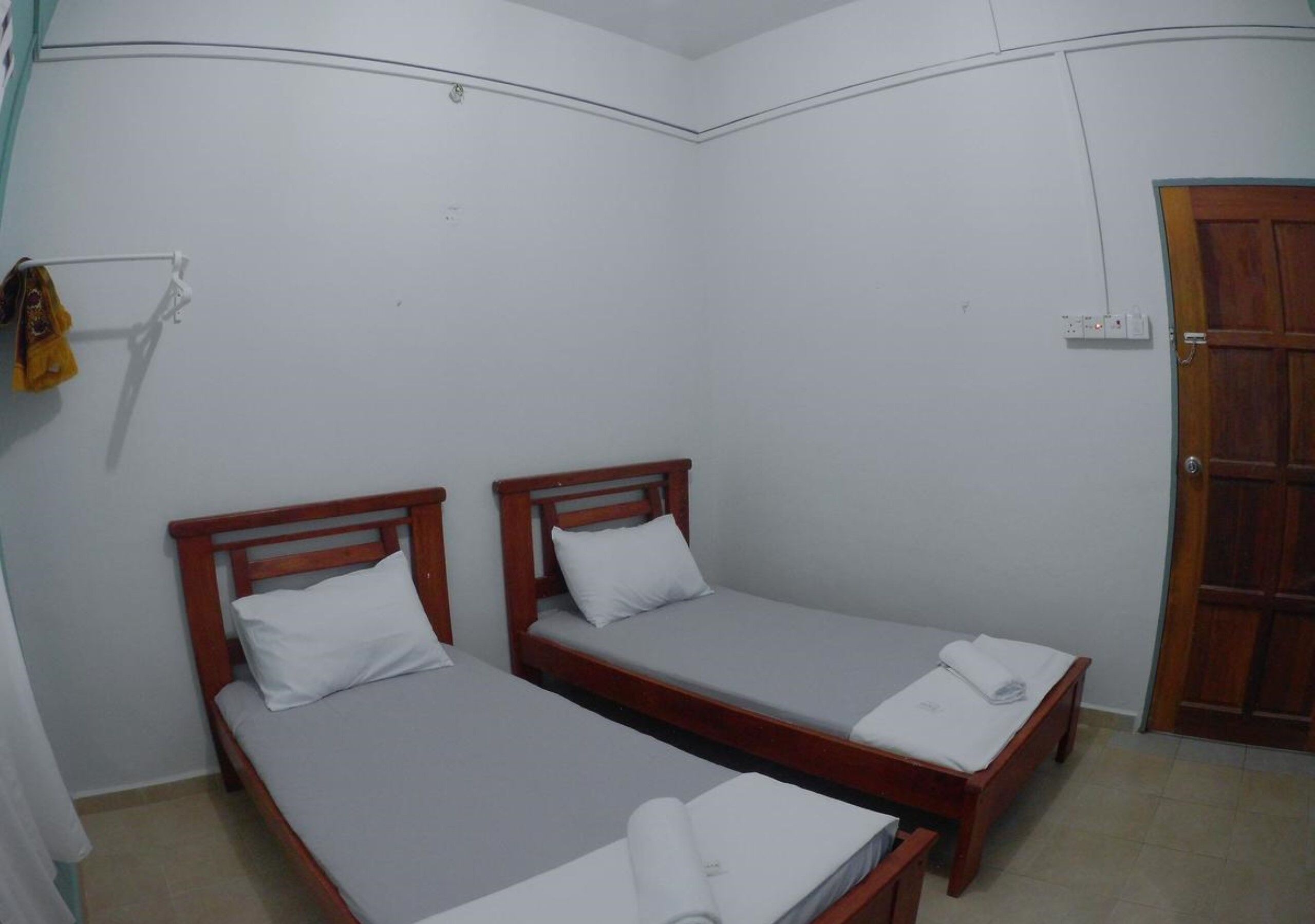 A small, clean room with two wooden beds, a wooden door, and a white wall.