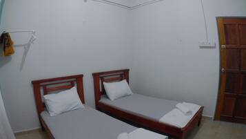 A small, clean room with two wooden beds, a wooden door, and a white wall.
