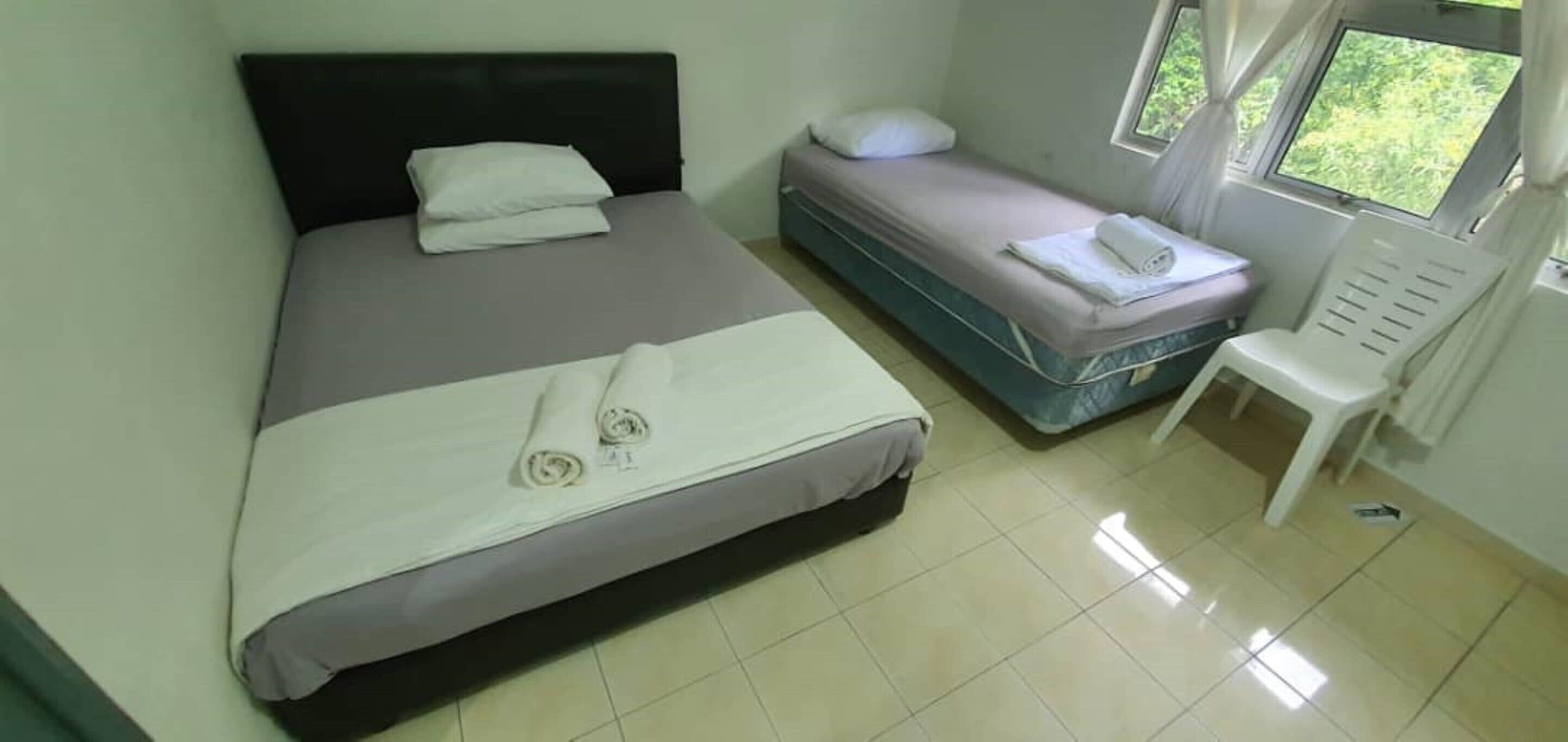Una stanza con un letto grande, un letto più piccolo, una sedia e una finestra con tende.
