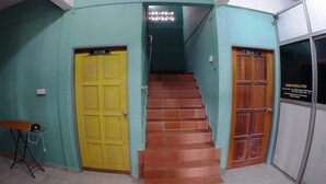 Una scala conduce a un secondo piano con pareti color verde acqua, una porta gialla con la scritta “SETOR” e una porta in legno con l’indicazione “BILIK 117”.