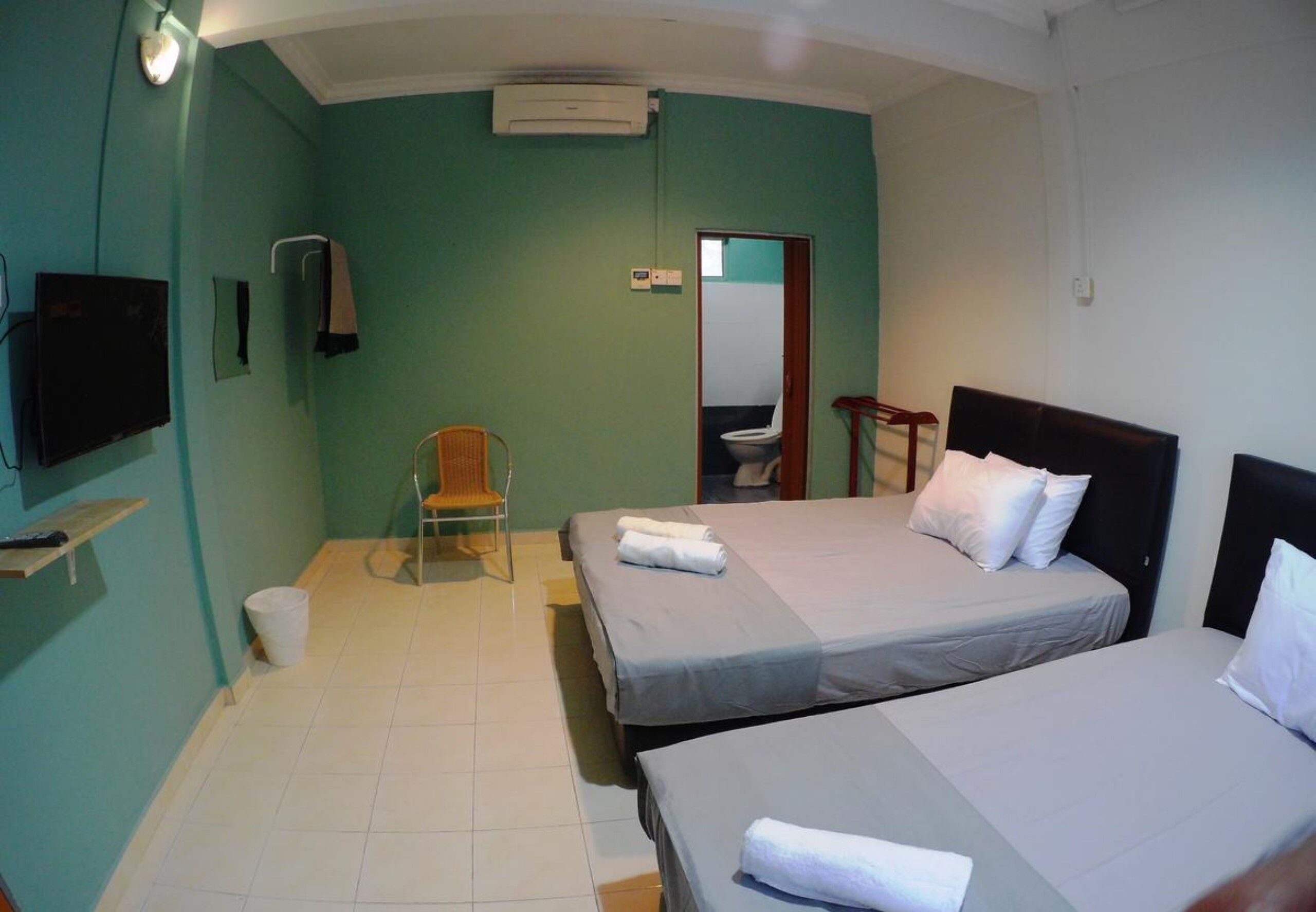 A room with two beds, a chair, a TV, and a bathroom visible through an open door.