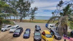 Un parcheggio alberato da palme con diverse auto e un furgone, e vista sulla spiaggia.