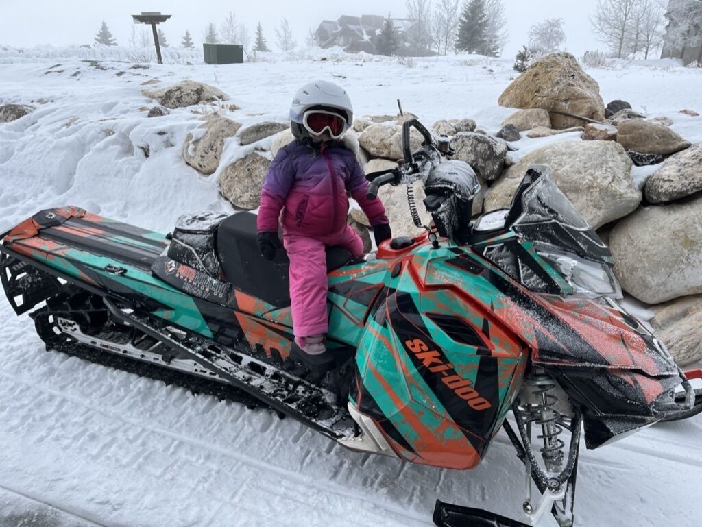 Un enfant sur une motoneige, portant un casque et des lunettes de protection, et vêtu d’une combinaison de ski rose.