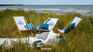 Deux chaises de plage, une couverture et des coussins sont disposés sur une pelouse près de l’océan.