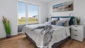 Une chambre moderne avec un grand lit, une vue dégagée sur l’extérieur grâce à une porte coulissante, et une décoration murale sur le thème de la plage.