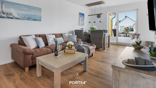 Un salon moderne avec un canapé marron, une table basse en bois, des fauteuils en osier et un coin repas comprenant une table et des chaises.