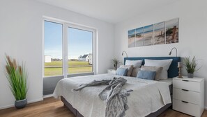 A modern bedroom with a large bed, a view through a sliding door, and a beach-themed wall art.