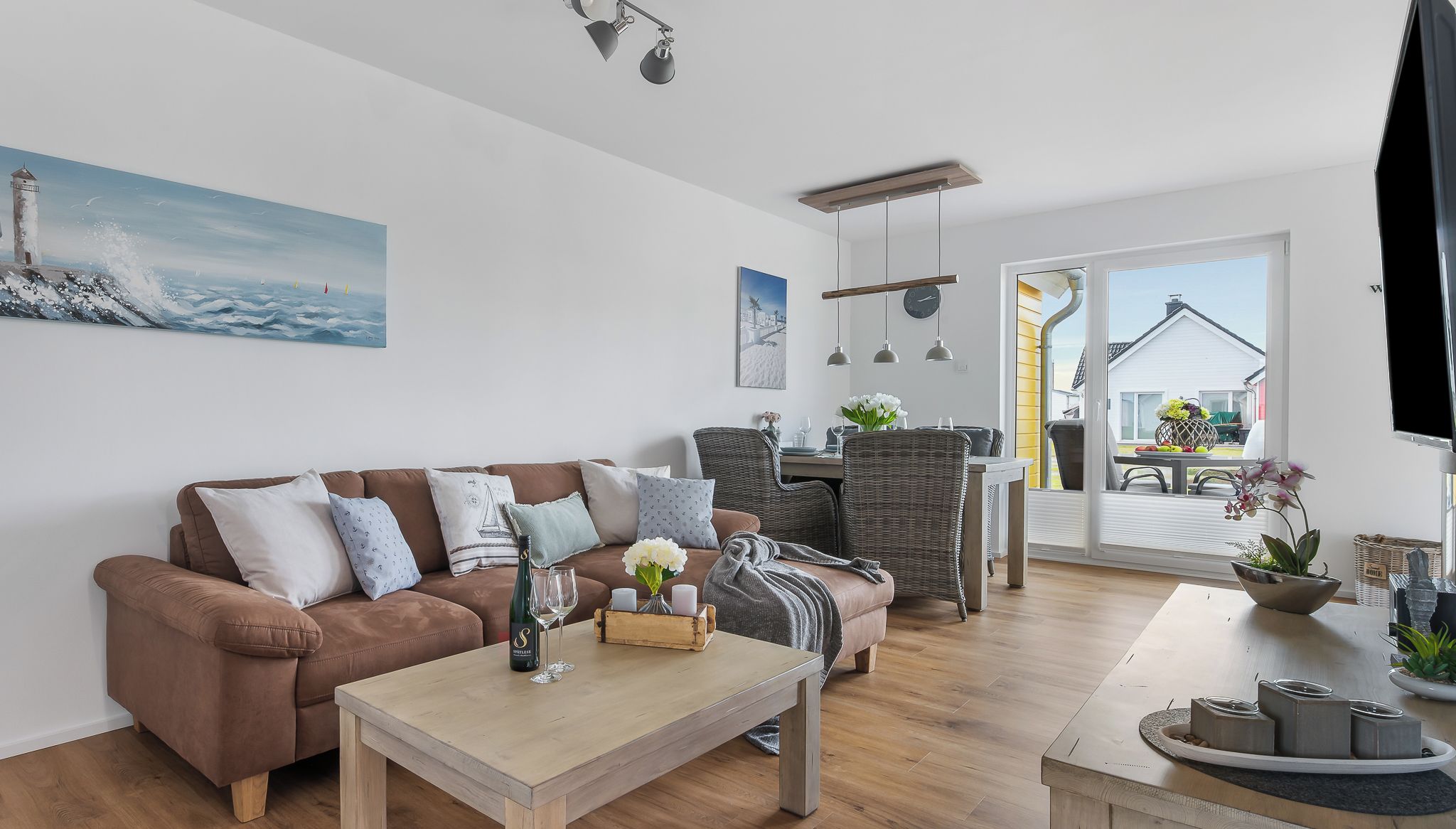 Uma sala de estar moderna com um sofá marrom, uma mesa de centro de madeira, cadeiras de vime e uma área de jantar com mesa e cadeiras.