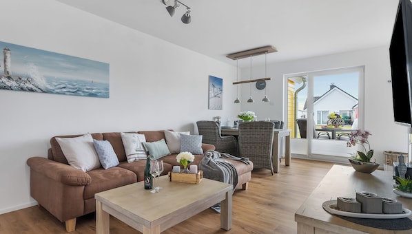 A modern living room with a brown sofa, a wooden coffee table, wicker chairs, and a dining area with a table and chairs.