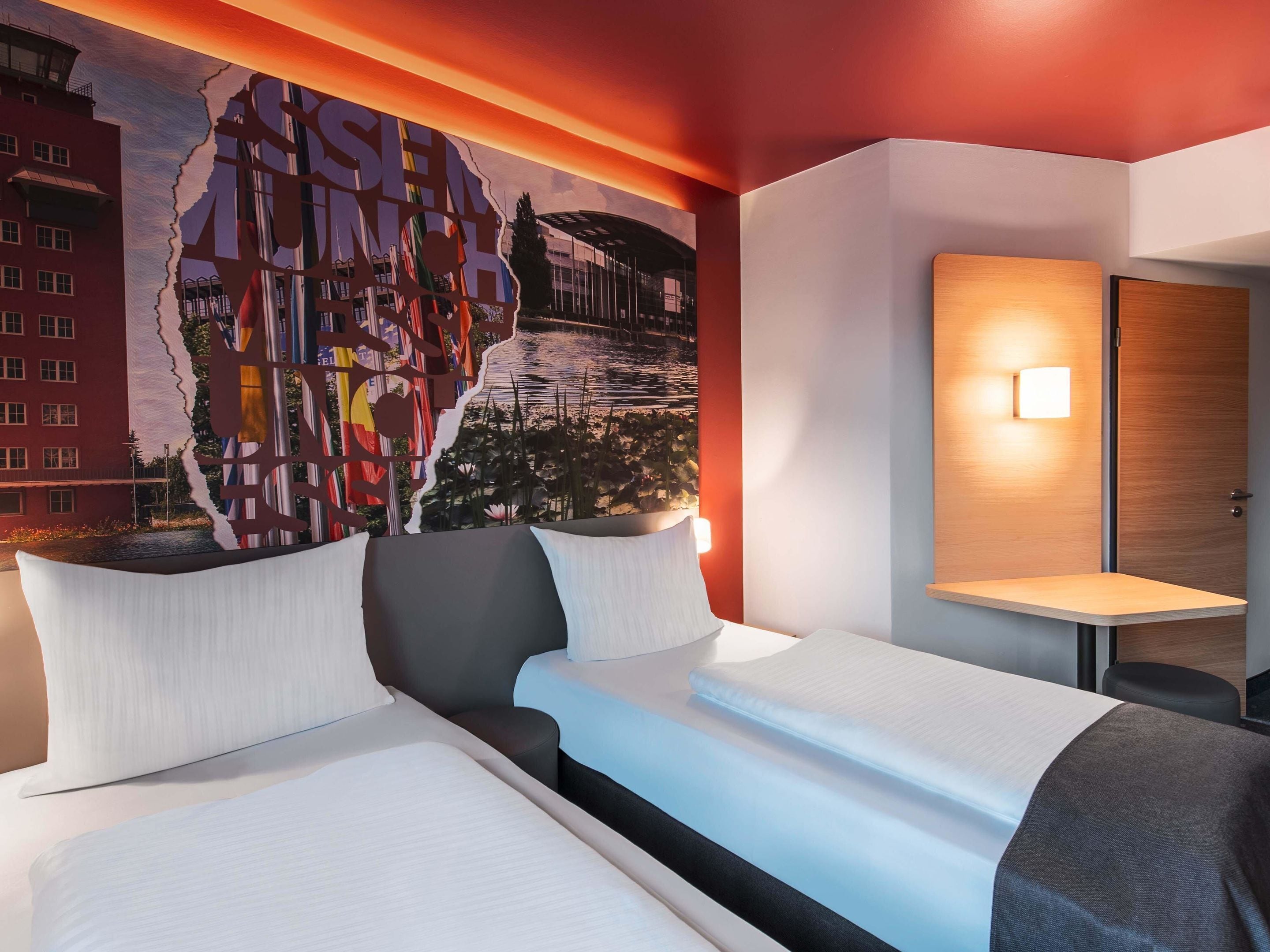 Ein Hotelzimmer mit einer großen Wandmalerei, einem Bett mit weißer Bettwäsche, einem Nachttisch mit einer Lampe und einer Holztür.