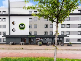 A B&B hotel with a modern facade, outdoor seating, and a tree in front.