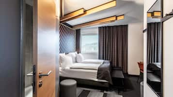 A modern hotel room with a bed, a desk, a chair, and a large window.
