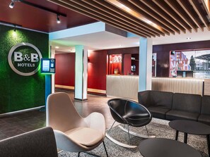 A hotel lobby with a reception desk, seating area, and a bar. - B&B Hotel München-Messe (Aschheim)