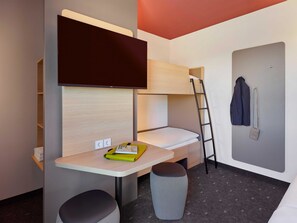 A compact hotel room with a bunk bed, a desk with a chair, a small stool, a wall-mounted TV, and a coat rack. - B&B Hotel München-Messe (Aschheim)