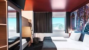 A modern hotel room with a bunk bed, a desk, and a large window offering a city view. - B&B Hotel München-Messe (Aschheim)