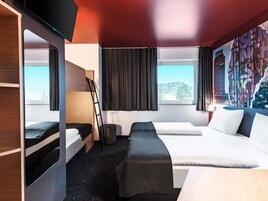 A modern hotel room with a bunk bed, a desk, and a large window offering a city view.