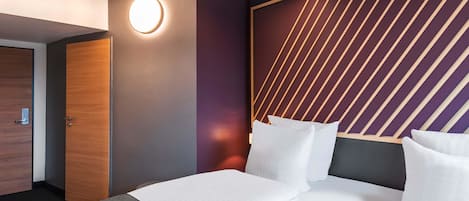 Habitación de hotel con diseño moderno, que presenta una cama grande con ropa blanca, cabecero de madera con líneas diagonales y una lámpara de pared circular.