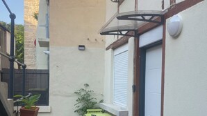 Een klein terras buiten, met een tafel, stoelen, een bloempot en een deur.