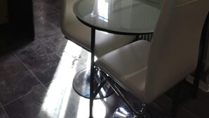 Een moderne eethoek met een glazen tafel, twee stoelen, een televisie en een raam met gordijnen.