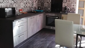 Een moderne keuken met een centraal eiland, roestvrijstalen apparatuur, een decoratieve spatwand en een hanglamp.