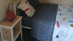 Een kleine, keurig ingerichte slaapkamer met een enkel bed, nachtkastje en een aan de muur bevestigd schilderij.
