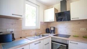 A compact kitchen with white cabinets, a built-in oven, a coffee maker, and a window providing natural light. - Ferienhaus Anja - FH Anja (Plau am See)