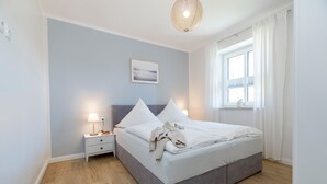 A bedroom with a bed, bedside table, lamp, and a window with curtains. - Ferienwohnung Junis, Deutschland (Sassnitz)