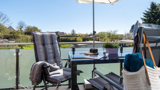 A balcony with a table, chair, umbrella, and a view of a river and buildings. - Ferienwohnung Junis, Deutschland (Sassnitz)