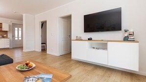 A modern living room with a wooden dining table, a white entertainment unit, and a flat-screen TV. - Ferienwohnung Junis, Deutschland (Sassnitz)