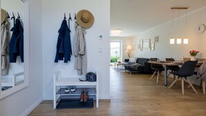 A modern living room with a dining area, wooden flooring, and a white wall with a hat and clothes hanging. - Ferienwohnung Junis, Deutschland (Sassnitz)