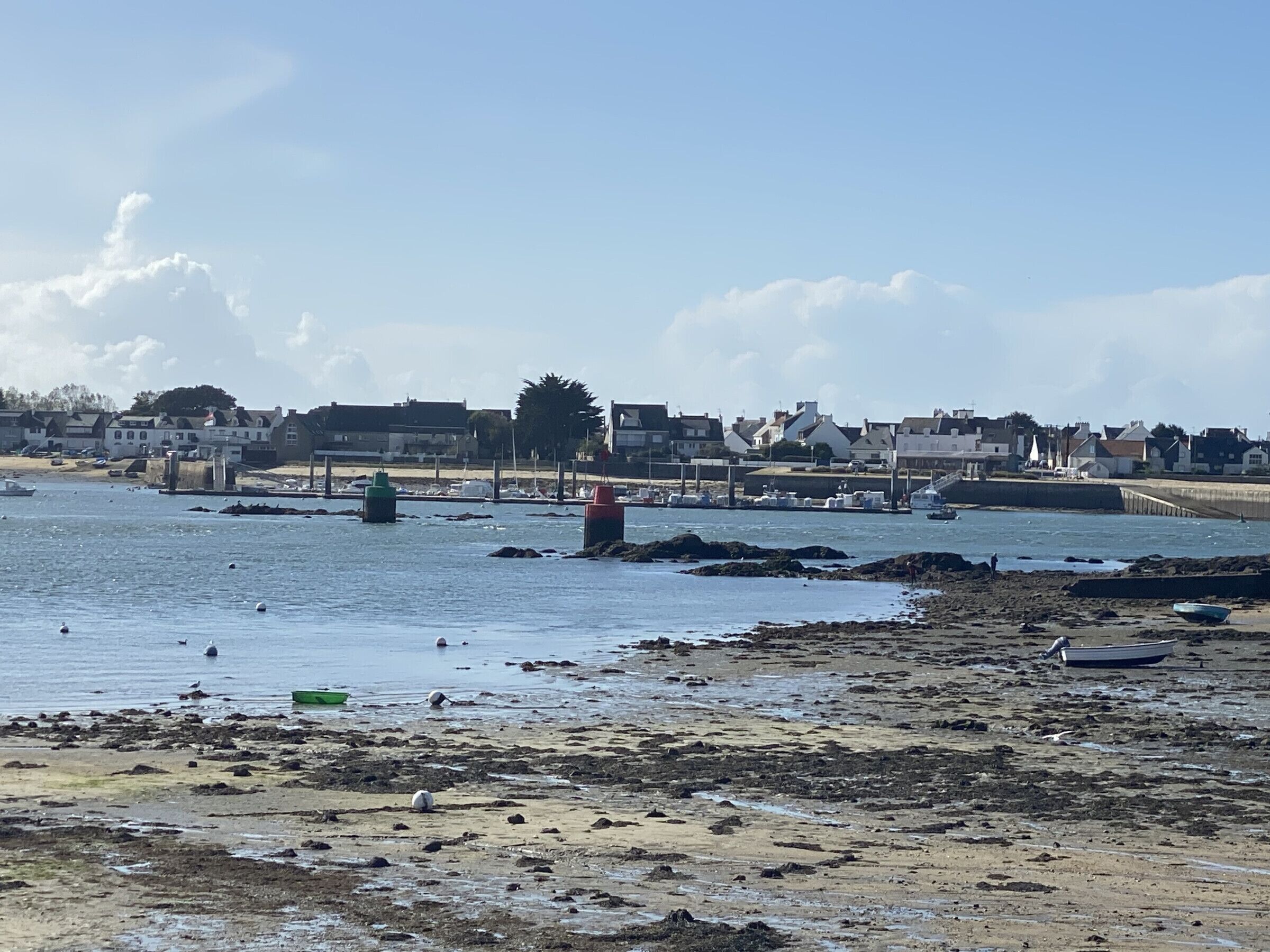 Escena costera con barcos, una playa arenosa y edificios al fondo.