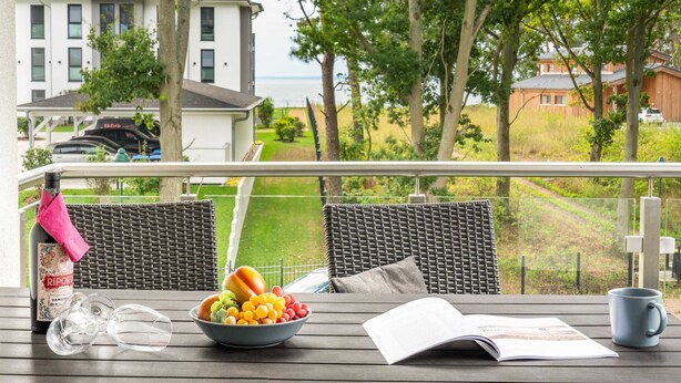 A balcony with wicker furniture, a bowl of fruit, a bottle of wine, and a magazine. - Apartment Kiefernblick - Haffresidenz (4a.7) - 4a.7 (Zirchow)