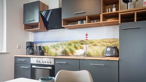 A modern kitchen with a built-in stove, a coffee maker, and a toaster. There is a window with a view of a beach and a lighthouse. - Apartment Kiefernblick - Haffresidenz (4a.7) - 4a.7 (Zirchow)