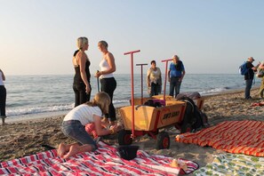 Eine Strandansicht mit Menschen, einem hölzernen Wagen und Decken.