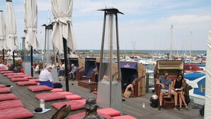 Una terraza con asientos acolchados rojos, una estructura metálica alta y vistas a barcos al fondo.
