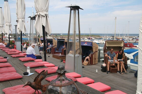 A deck with red cushioned seating, a tall metal structure, and a view of boats in the background. - HB Landhaus am Bauernhof in Ostseeland - 4-room country house with barbecue terrace (Kröpelin)