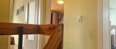 Un escalier avec des rampes en bois mène à une pièce dont les murs sont ornés de motifs jaunes et qui est éclairée par un luminaire au plafond.