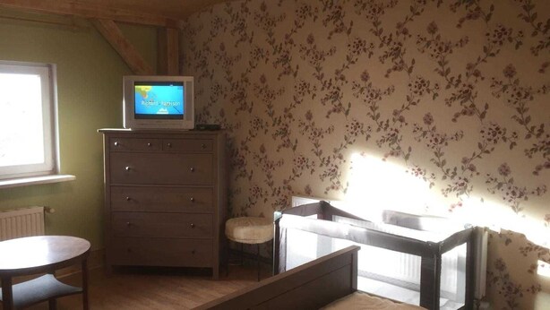 Una habitación con un aparador de madera, un televisor encima, una mesa redonda y un ventanal con papel tapiz floral.
