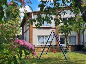 A residential building with a brick facade, a white window, and a swing set in the yard.