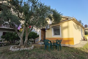 A small yellow building with a window and a door, surrounded by a garden with a tree and flowers. - Kuca sa vrtom za samostalnu upotrebu (Bibinje)