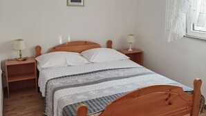 A single bed with a wooden frame, two bedside tables with lamps, a framed picture on the wall, and a window with sheer curtains.