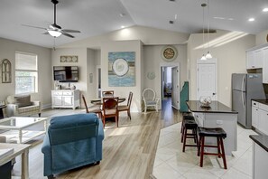 A spacious living room with a blue sofa, dining area, kitchen, and a ceiling fan.