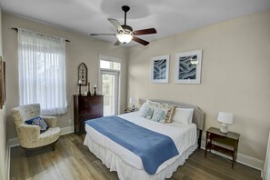 A bedroom with a large bed, a ceiling fan, a chair, a dresser, and two wall-mounted lamps.