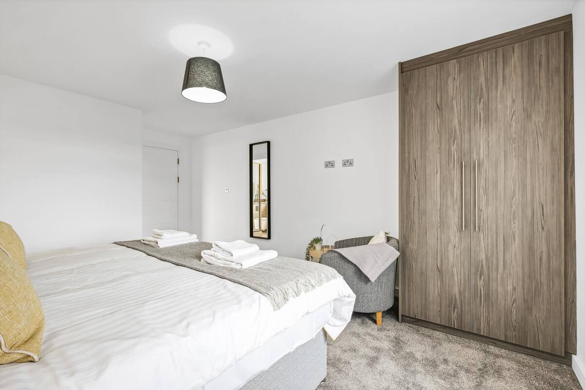 Un dormitorio moderno con una cama grande, un armario, una mesita de noche con una lámpara y un espejo en la pared.